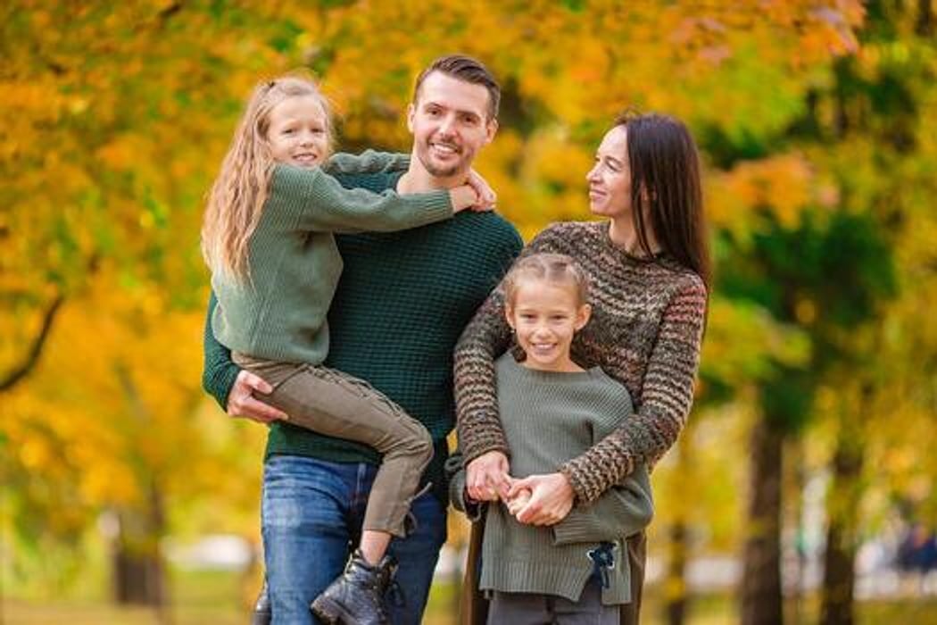 Smiling parents carrying their two daughters through a golden autumn park