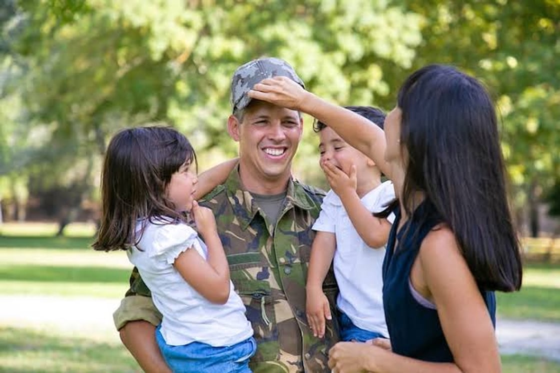 Smiling service member in the park with his wife and two young children
